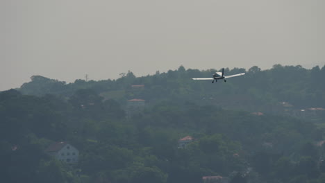 small single engine training airplane with visible landing gear flying above green hills and rural houses
