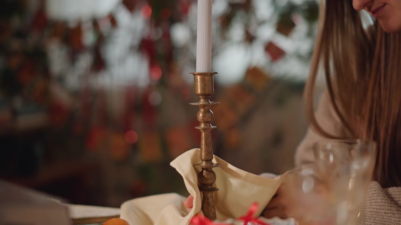 Woman arranging candlestick with napkin, crystal glass and bowl of berries nearby, warm foliage backdrop, intimate host preparing seasonal setting, gentle smile and reflective motion, cinematic