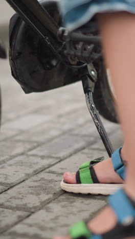 un primer plano de las piernas de un niño con sandalias de colores y pantalones cortos de jean azul mientras se mueve y monta la bicicleta