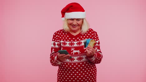 Christmas-grandmother-using-credit-bank-card,-smartphone-while-transferring-money-shopping-online