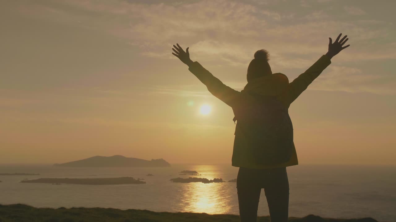 viajera femenina con mochila de pie con los brazos levantados en el acantilado
