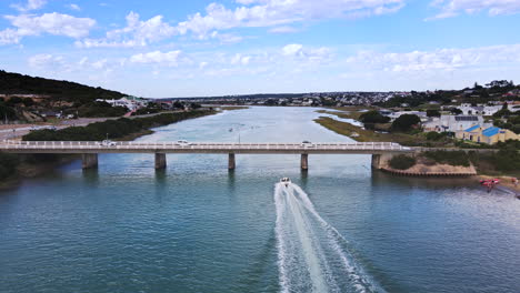 aerial riser view of motorboat speeding by on goukou river under stilbaai bridge