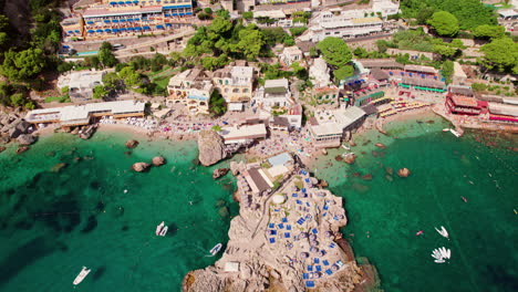 Eine-Epische-Luftaufnahme,-Die-über-Atemberaubende-Strände-Und-Glitzerndes-Blaues-Wasser-In-Marina-Piccola-Auf-Capri-Kreist,-Einer-Berühmten-Insel,-Die-Ein-Beliebtes-Luxusurlaubsziel-In-Italien-An-Der-Amalfiküste-Ist