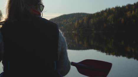 woman paddling canoe on beautiful lake in autumn, rear view closeup slow motion