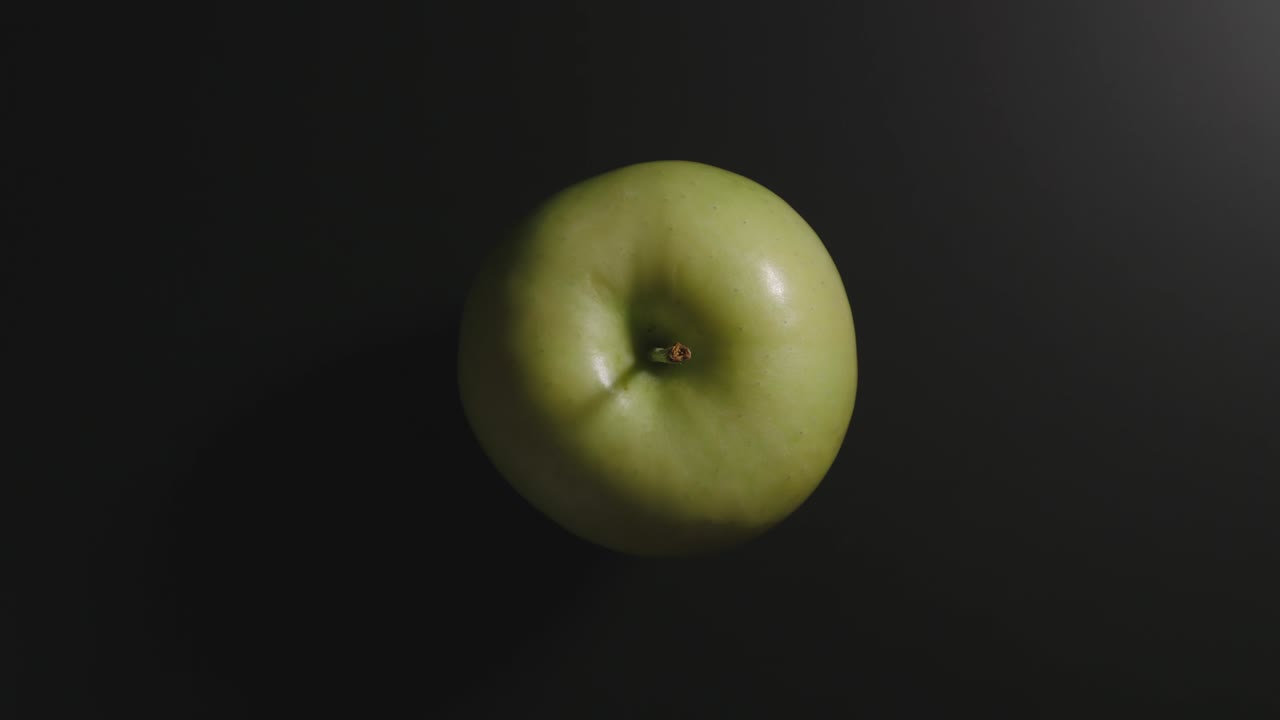 зеленое яблоко на черной поверхности. вид сверху. остановка движения