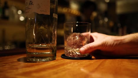 hand swirling ice in a glass tumbler