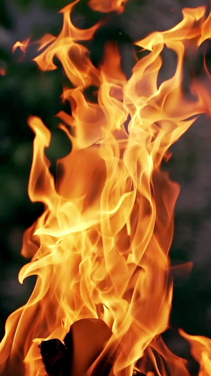 Big fire flame with dark smoke outdoors. Bright flame glowing with red and yellow colors near the house in the evening. Vertical video