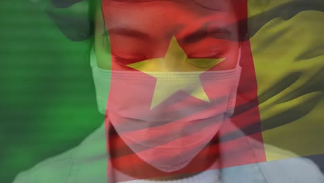 Animation-of-flag-of-cameroon-waving-over-woman-wearing-face-mask-during-covid-19-pandemic