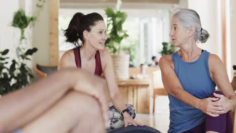 happy diverse seniors sitting in pilates class talking with female coach, unaltered, in slow motion
