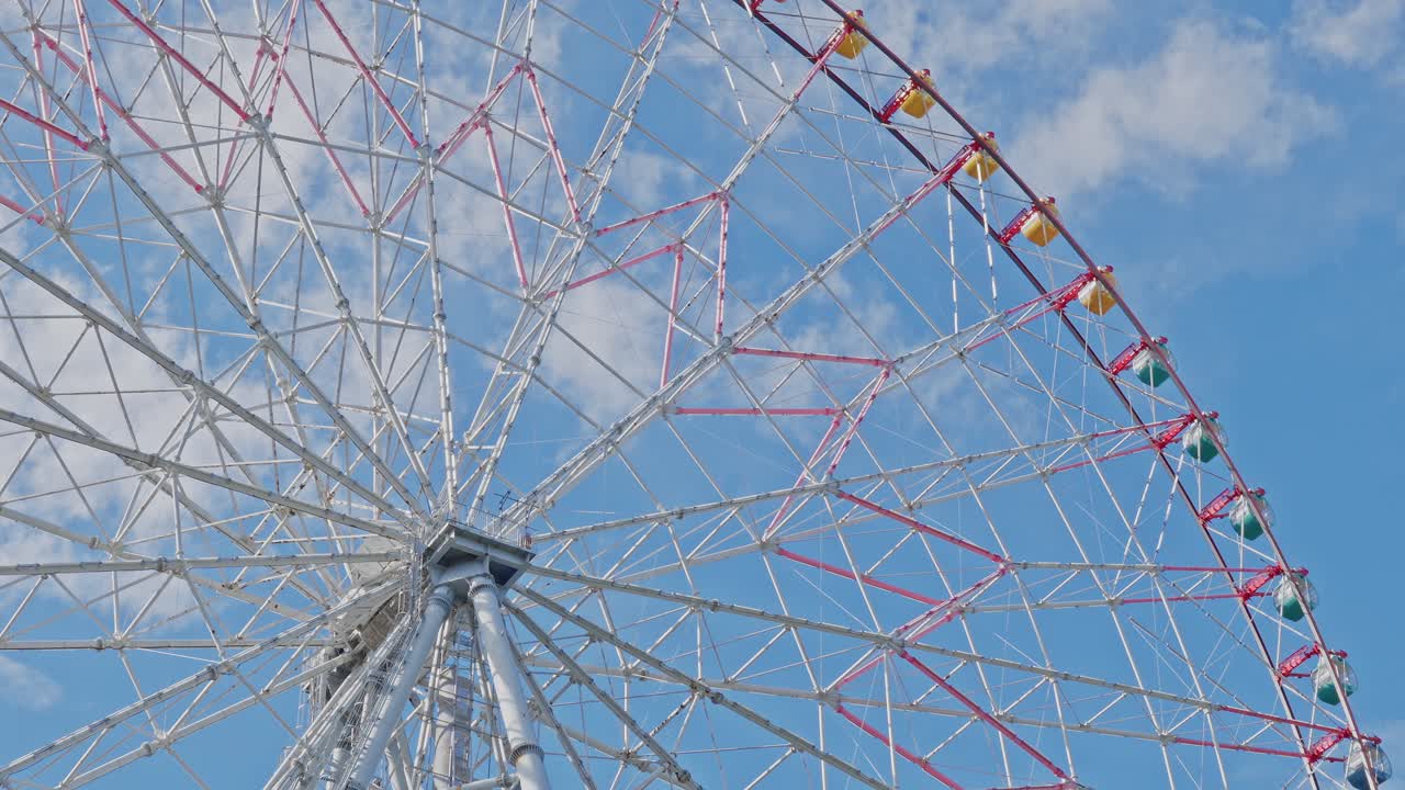 Detailed view of the intricate white and red spoke structure and central hub of a large Ferris wheel against a cloudy blue sky