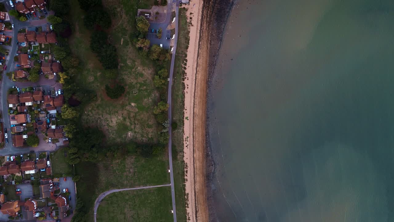Birds-eye aerial moves forward over Weston Shore beach Southampton, with autumn trees, calm shoreline, and warm sunset colors casting a golden glow across the coastal landscape