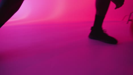 silueta de estudio de cerca de un jugador de baloncesto masculino driblando y rebotando la pelota contra un fondo iluminado de color rosa