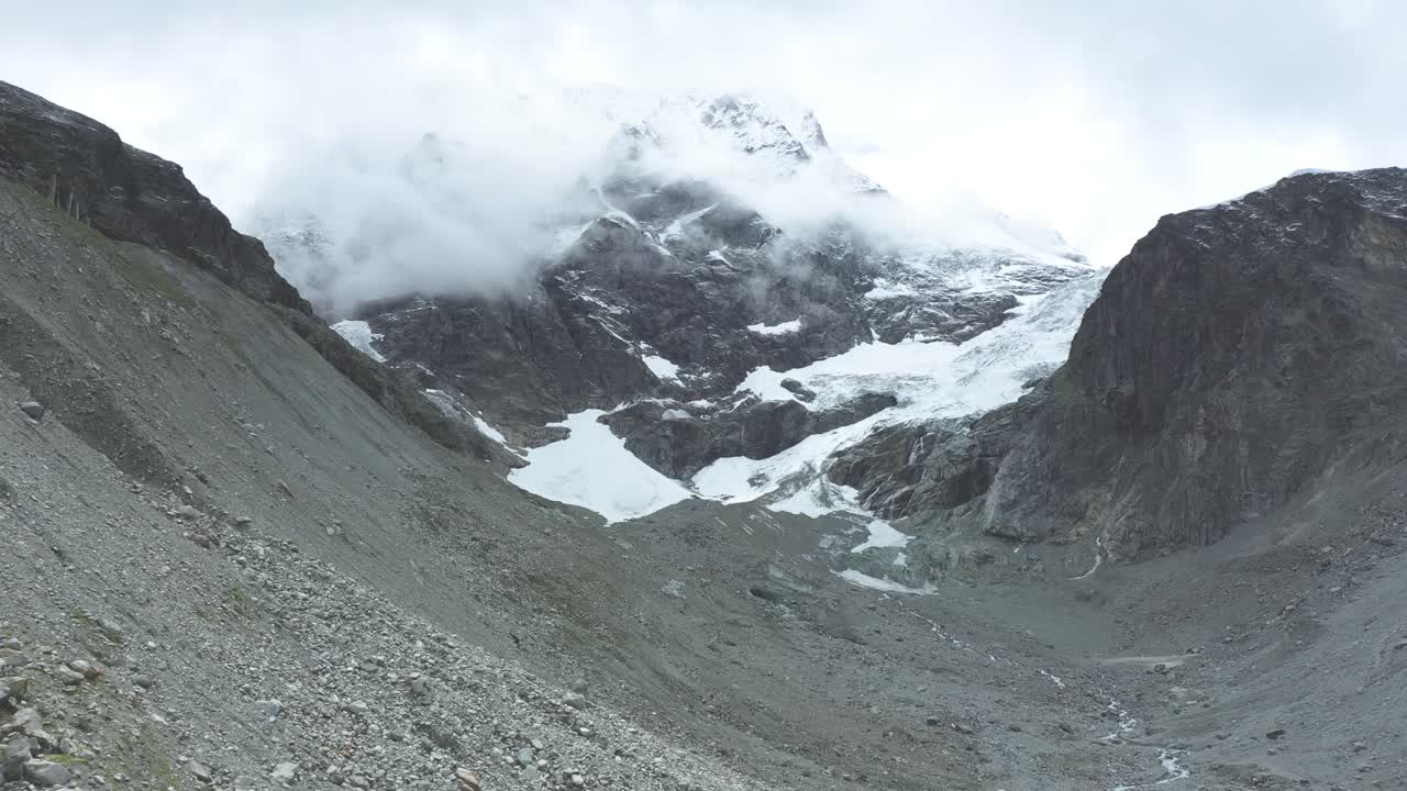 vista de drones sobre un desolado glaciar alpino en retroceso rodeado de montañas y rocas y picos cubiertos de nieve