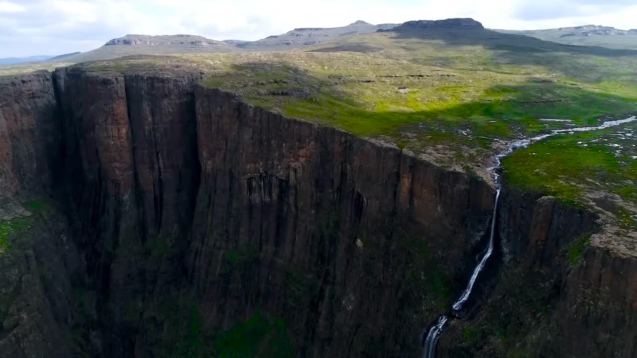 Aerial drone flying over and towards Tugela falls waterfall in South Africa during a sunny day while the water is falling down from a large and very high altitude cliff. Landscape is green and scenic.