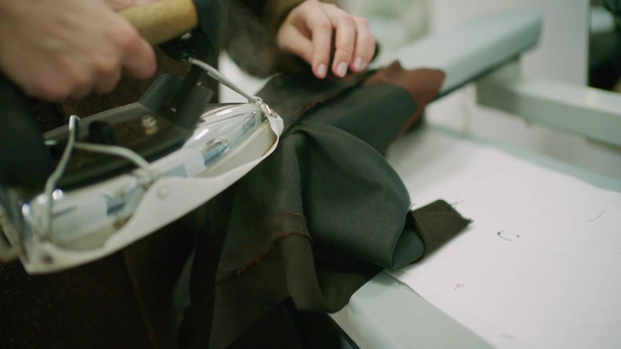Close up of a tailor using a professional steam iron on black fabric in a fashion workshop