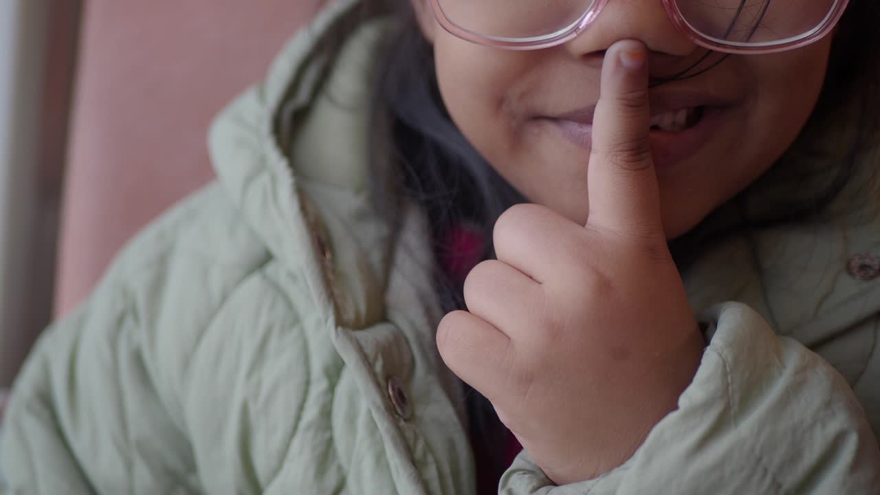 niña pequeña callándose con el dedo en la nariz