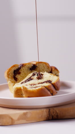 vertikales close-up-video von geschmolzener schokoladensauce, die auf ein schokoladen-babka-brötchen auf einem teller gegossen wird