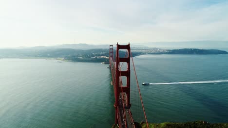 golden gate bridge and boat moving across still ocean under soft morning light