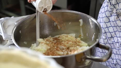 Cook-Adding-Seasoning-On-Casserole-Of-Cooked-Onions-In-The-Kitchen---Handheld,-Close-Up