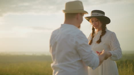 una pareja feliz baila y gira juntos al atardecer, ambos vestidos con camisas blancas y con sombreros. la cálida luz del atardecer mejora su momento alegre, creando una escena romántica y serena