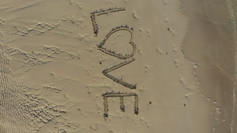 aerial crazy turning shot of love inscribed in the sand on a beach