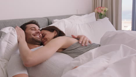 행복한 젊은 커플이 침대에 누워  ⁇ 안고 로맨틱한 관계를 나누고 집에서 함께 친밀감을 즐기고 있습니다.