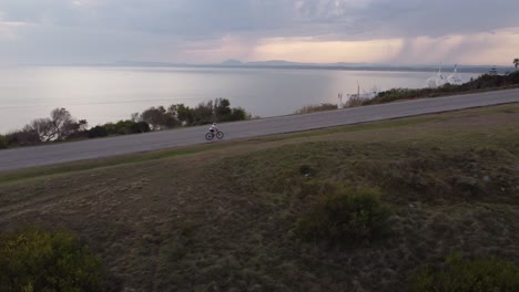 Man-riding-bicycle-reaching-the-top-of-slope-front-to-Ocean