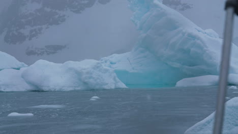 Eisberg-Und-Küste-Der-Antarktis-An-Einem-Verschneiten-Tag,-Blick-Vom-Boot-Aus,-Das-Im-Kalten-Ozeanwasser-Segelt