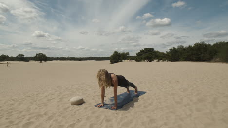 woman exercising yoga, doing upward facing dog in sand dunes with forest