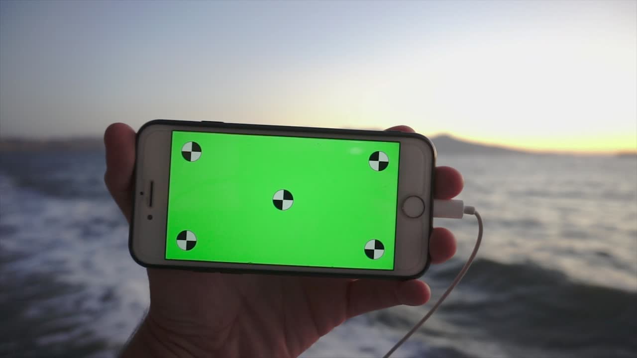 크롬 키와 함께 회전하는 스마트폰, 녹색 화면. 알파 비디오, 나무 바탕에 휴대 전화.