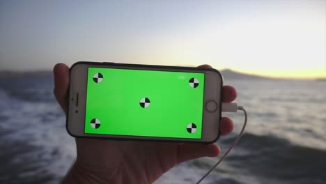 teléfono inteligente girando con llave de cromo, pantalla verde. video alfa, teléfono móvil en fondo de madera.