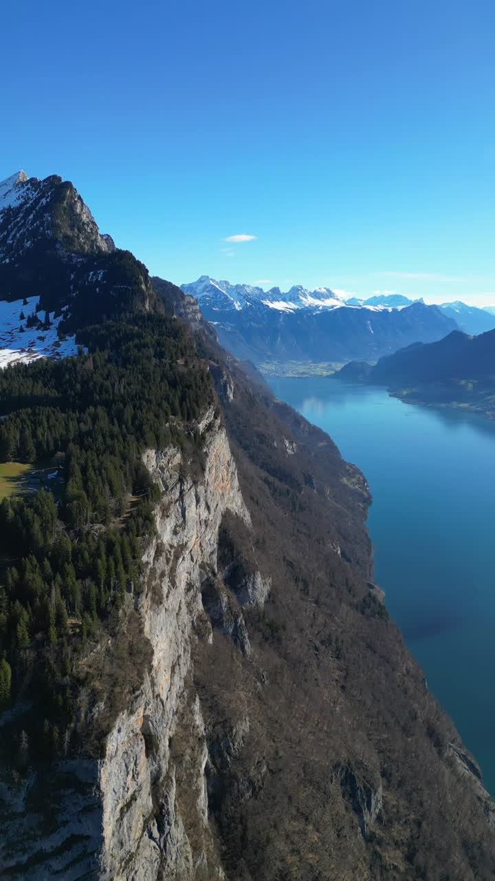 Churfirsten-vuorten kalkkikivikallion juurella Walen-järvellä (Walensee) Sveitsissä, pystysuuntainen ilmakuvausvideo.