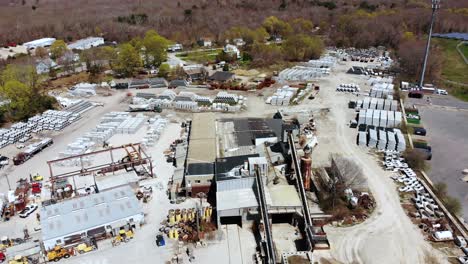 a daytime drone view of a cement manufacturing plant showing a construction yard full of cement pipes and other forms, as trucks and people move around below