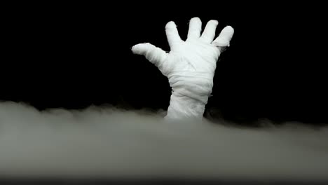 terrible mummy hand rising out from the smoke at black background. slow motion