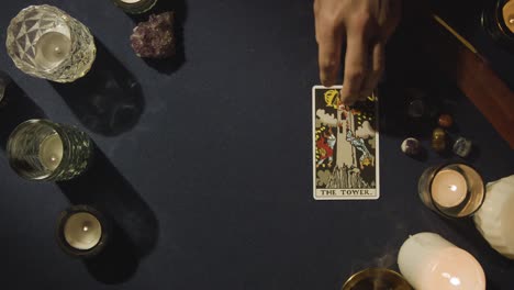 overhead shot of person giving tarot card reading laying down the tower card on table