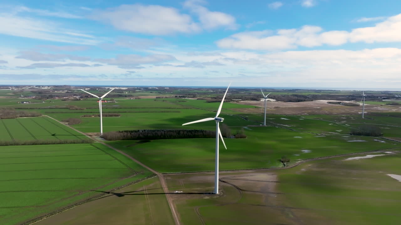 Aerial drone shot of wind turbines amidst wet, green fields during early springtime