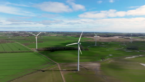 aerial drone shot of wind turbines amidst wet, green fields during early springtime