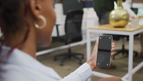 feliz mujer de negocios afroamericana usando un teléfono inteligente con espacio de copia en la oficina