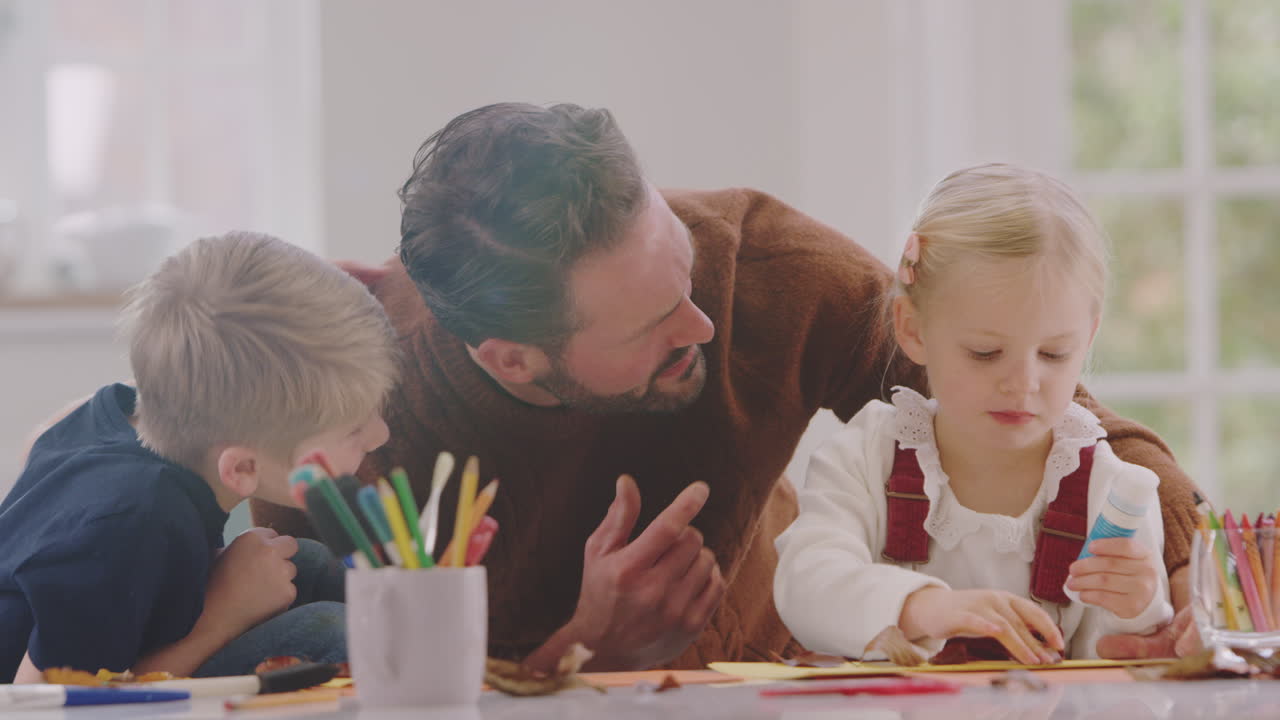 Vater mit Kindern zu Hause beim Basteln und Blätterbilder machen in der Küche