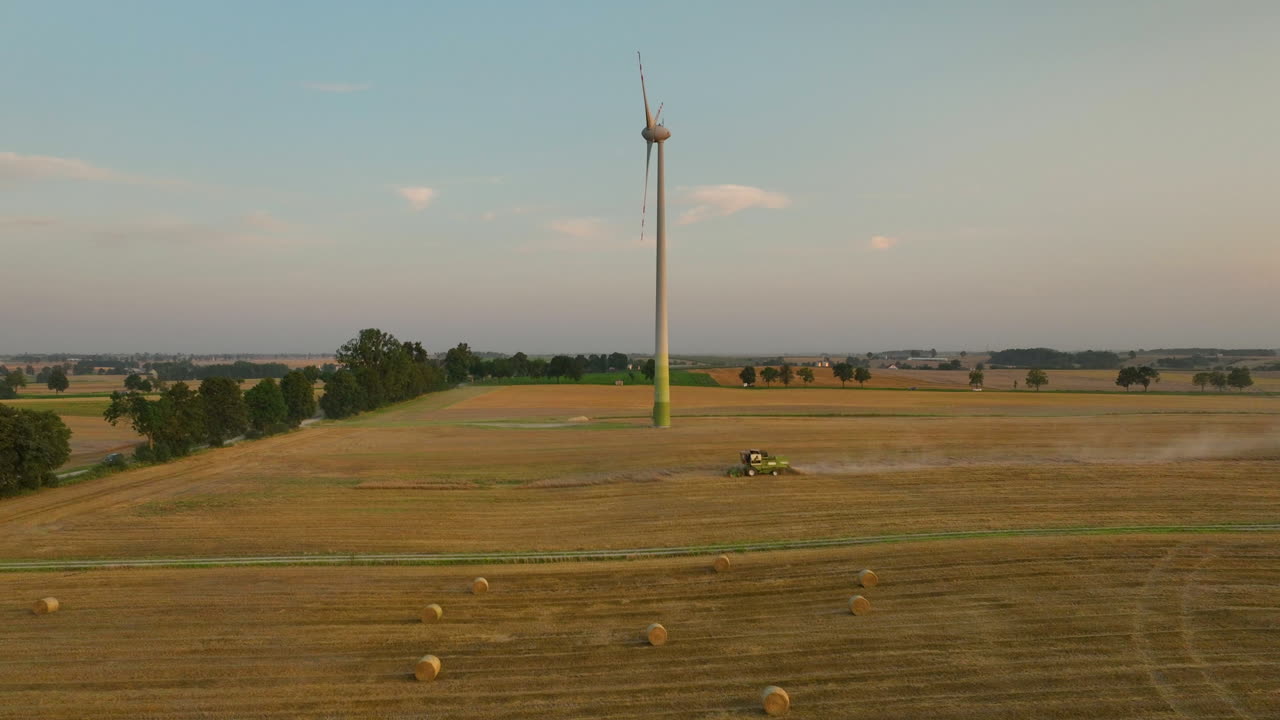 Wind turbine with combine harvester working on farmland during harvest, renewable energy and agriculture