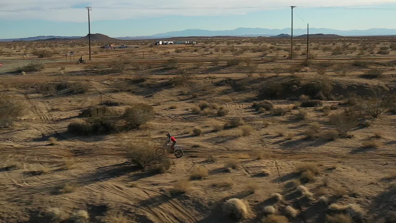 motociclista todoterreno recorriendo un sendero lleno de baches en el desierto de mojave y luego saltando un camino de tierra - vista aérea en cámara lenta