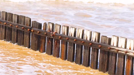 dynamic waves hit a wooden barrier along the great ocean road, captured in bright daylight with a steady camera