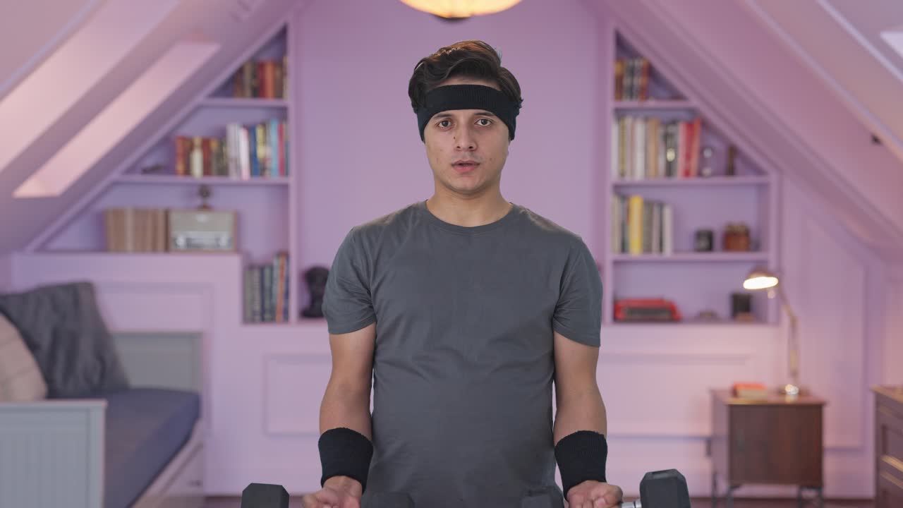 인도인 남자가 무거운 덤벨을 들어 올리고 운동을 하고 있습니다.