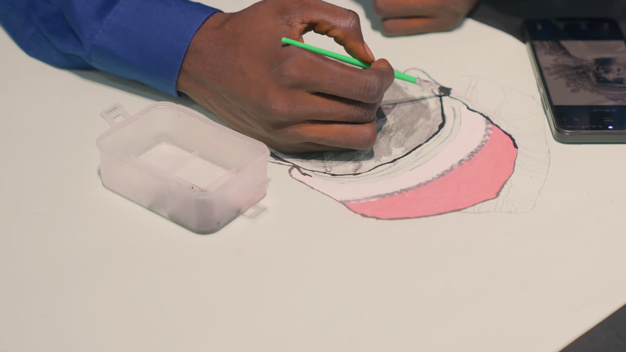 Macro shot of black illustrator refining portrait, green handled brush, precision shading and tiny ink dots, smartphone reference image at side, concentrated hands, studio lighting highlighting