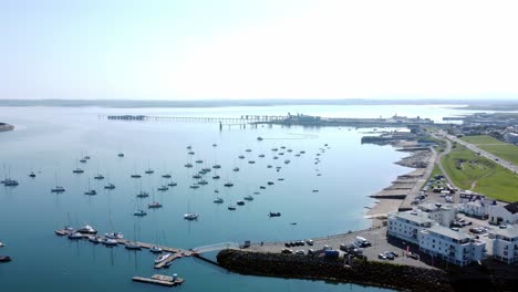 sunny holyhead harbour breakwater maritime yachts docked along transparent calm blue shoreline aerial descending view