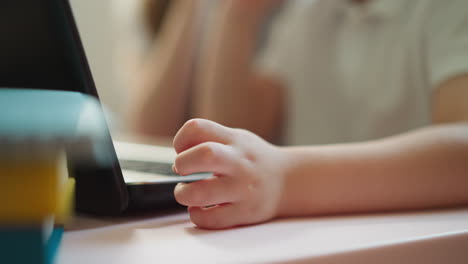 little schoolboy hand rests near laptop on wooden desk