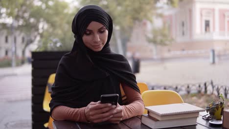Junge-Muslimische-Frau-In-Schwarzem-Hijab-In-Entspannter-Atmosphäre-Im-Café-Im-Freien