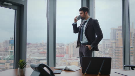 serious manager enjoy coffee break standing at window office. man holding cup