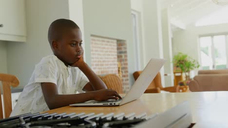 Vista-Lateral-De-Un-Niño-Negro-Usando-Una-Computadora-Portátil-En-La-Mesa-Del-Comedor-En-Una-Casa-Cómoda-4k