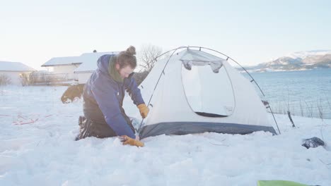 camper assembling camping tent on snowy ground by the river